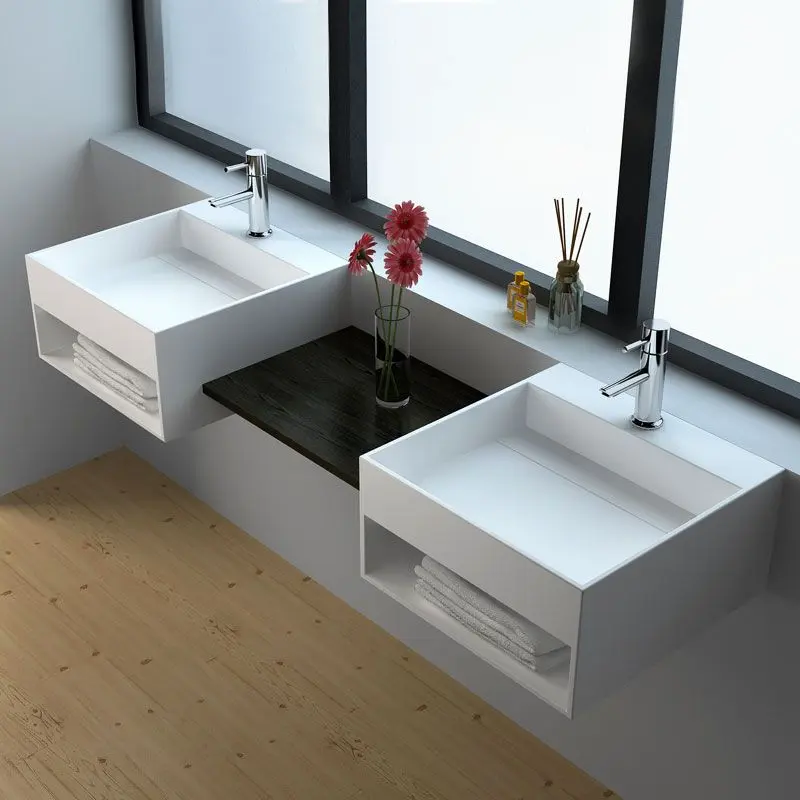 Double lave-mains suspendus design blanc avec espace de rangement intégré pour serviettes sous la vasque dans une salle de bain moderne.