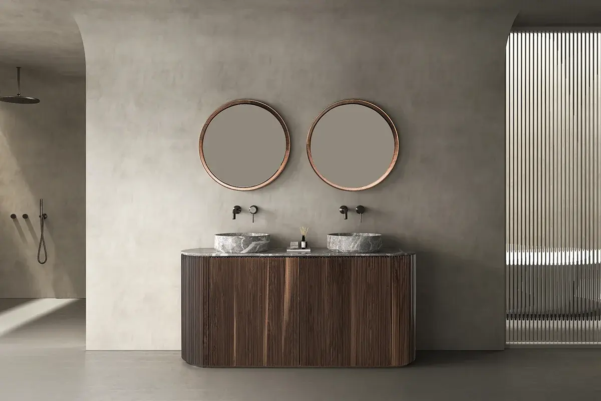 Ensemble salle de bain élégant composé d’un meuble oblong cannelé en finition noyer Black de 160 cm, surmonté d’un plan en marbre véritable accueillant deux vasque à poser en marbre Casso Grey. Deux miroirs ronds de 65 cm de diamètre, encadrés de bois noyer, complètent la composition avec harmonie. L’ensemble joue sur les matières nobles et les formes douces pour une salle de bain à l’esthétique organique et contemporaine.
