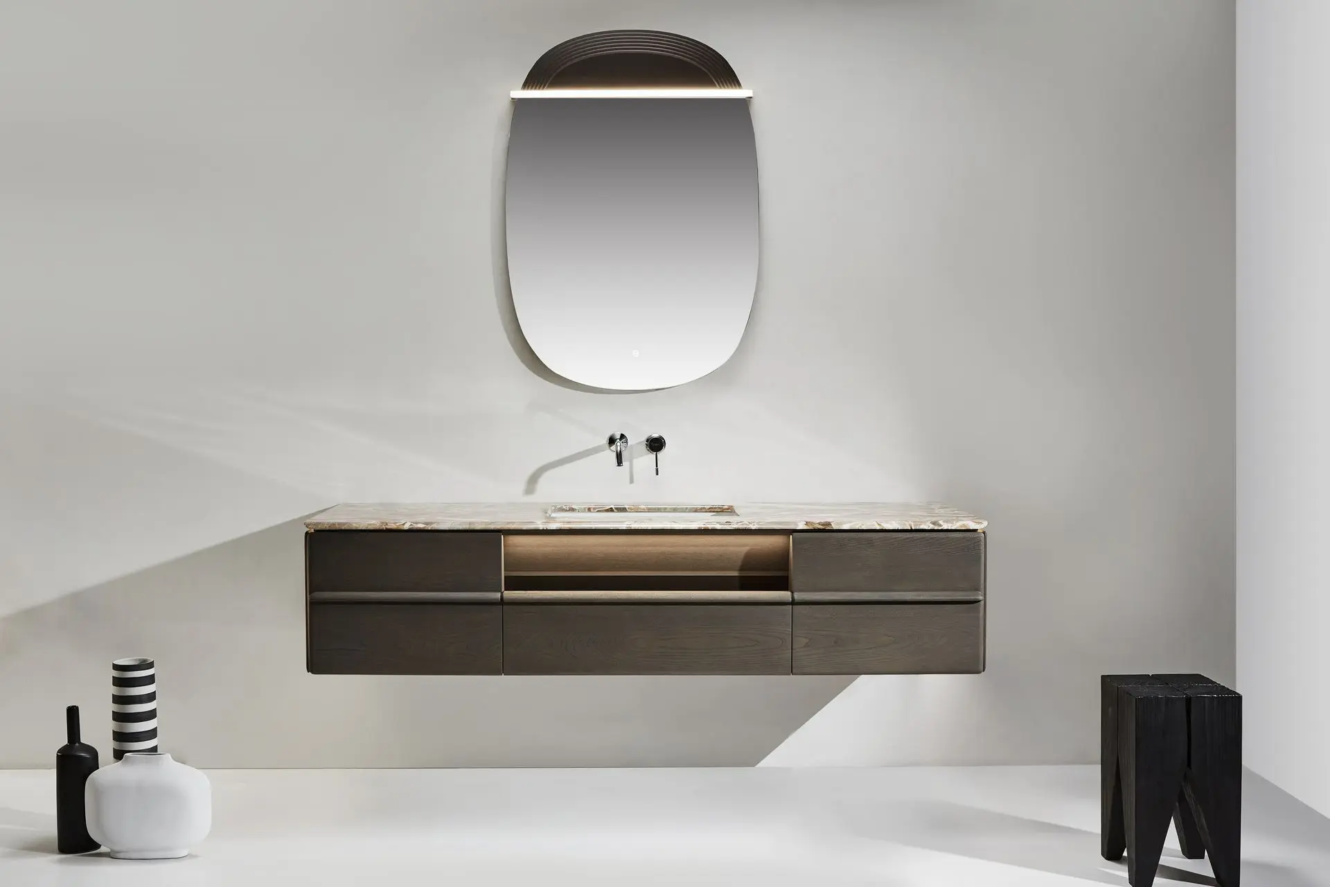 Ensemble de salle de bain composé d’un meuble vasque suspendu en bois fumé, surmonté d’un plan en marbre véritable de 180x60 cm. La vasque en céramique est discrètement encastrée, et un miroir LED à cadre bois (75x106 cm) complète l’ensemble, apportant une touche de modernité et de chaleur à l’espace.