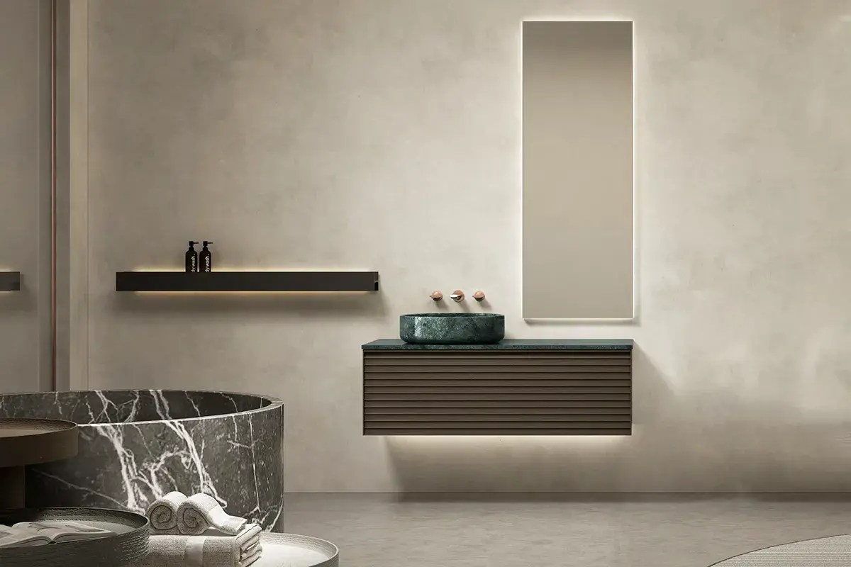 Ensemble de salle de bain compact et design composé d’un meuble asymétrique en noyer cannelé (120x55 cm), surmonté d’un plan en marbre véritable vert Jade avec une vasque à poser coordonnée. L’asymétrie apporte une touche contemporaine et architecturale, tandis que le miroir LED vertical (52x140 cm) avec cadre en bois vient souligner l'élégance naturelle de l'ensemble.