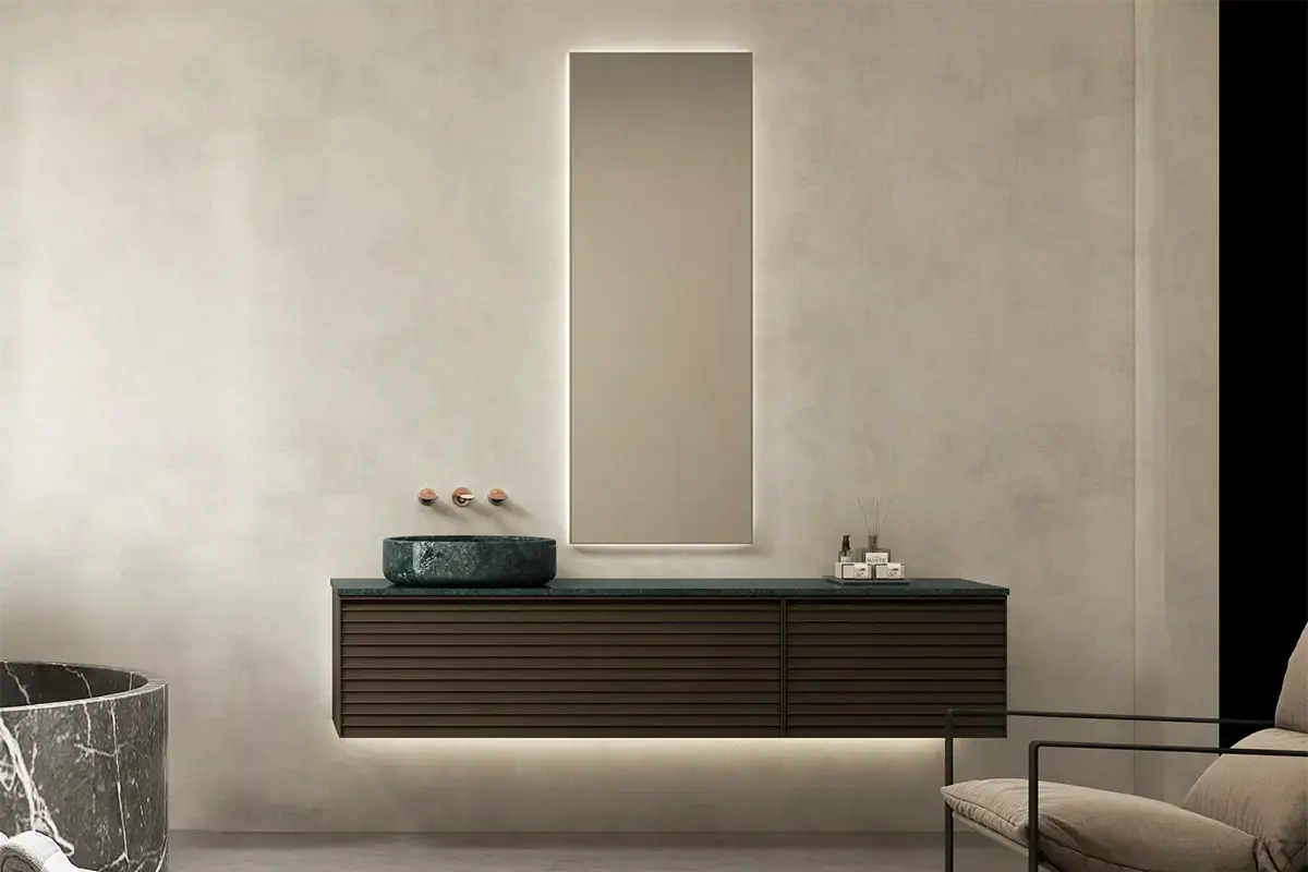 Ensemble salle de bain au design audacieux composé d’un meuble asymétrique en bois cannelé noyer (180x55 cm), surmonté d’un plan en marbre véritable vert Jade avec deux vasques à poser assorties. L’asymétrie subtile du meuble crée un jeu de volumes élégant et contemporain. Le miroir LED vertical (52x140 cm) encadré de bois complète l’ensemble avec une touche graphique et lumineuse.