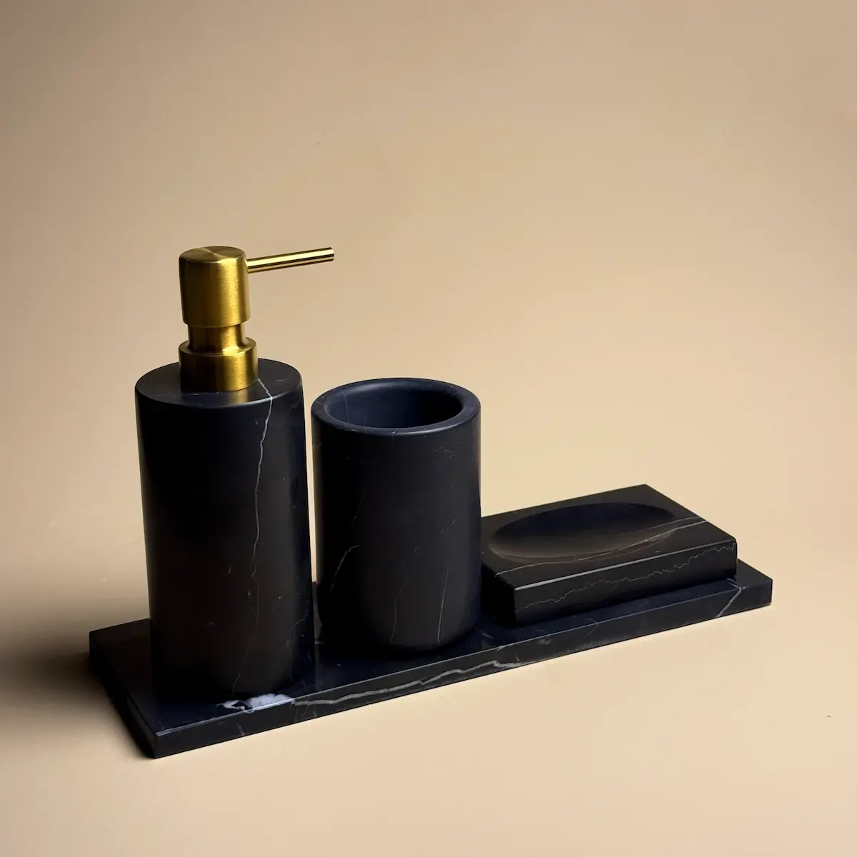 Vue de face du kit d'accessoires de salle de bain Yilstone Nero Marquina, présentant un distributeur de savon, un pot et un porte-savon sur un plateau rectangulaire en marbre noir veiné.